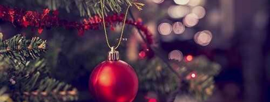 Closeup of red bauble hanging from a decorated Christmas tree. Retro filter effect.